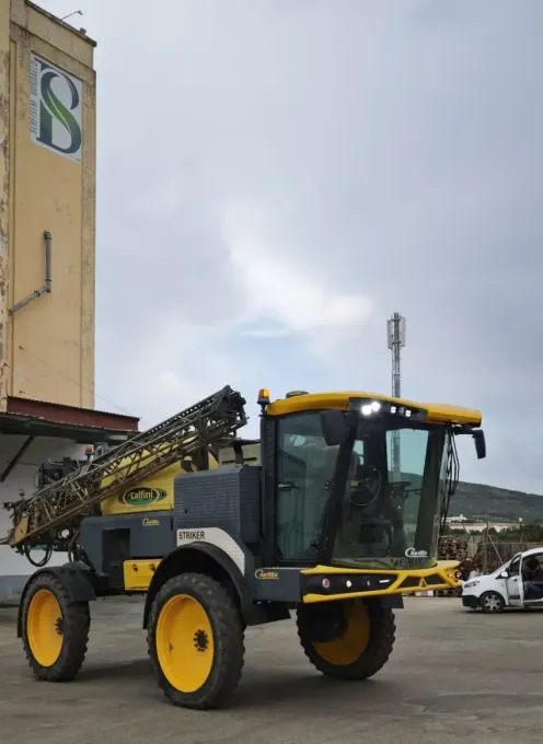 Máquina agrícola amarilla estacionada frente a un edificio en un día nublado.