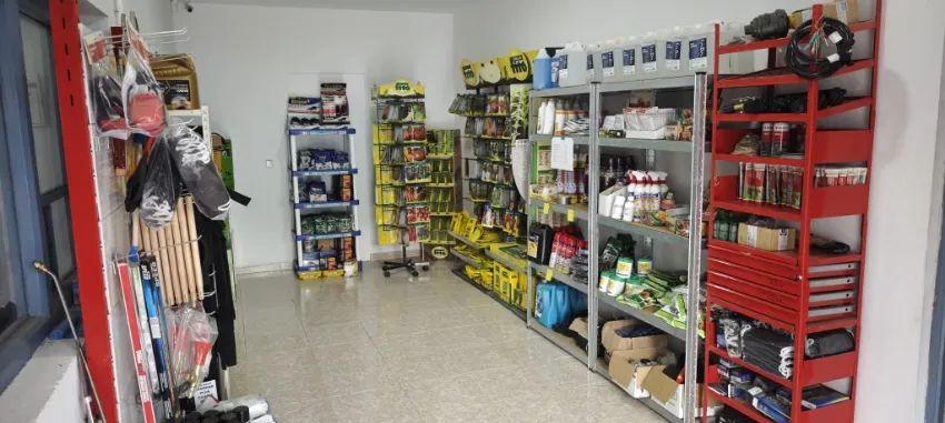 Interior de un pequeño pasillo de una tienda con estantes repletos de aperitivos, bebidas y artículos para el hogar.