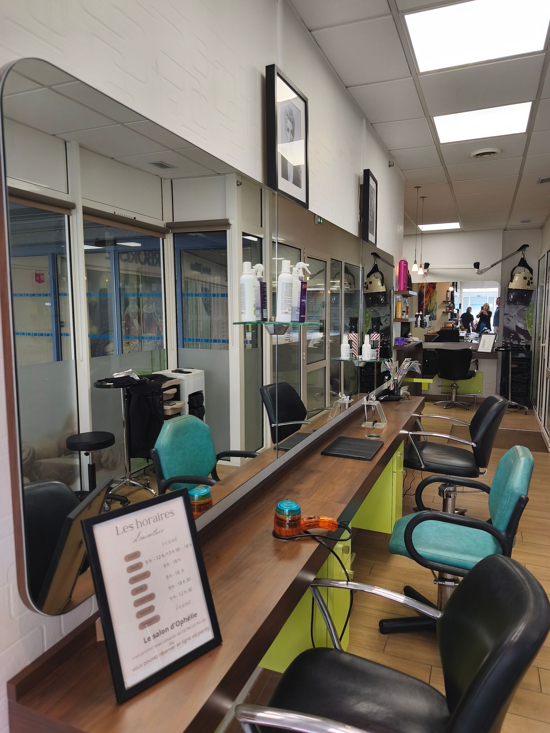 Intérieur d'un salon de coiffure avec fauteuils de coiffure, miroirs et étagères à produits le long d'une allée étroite.