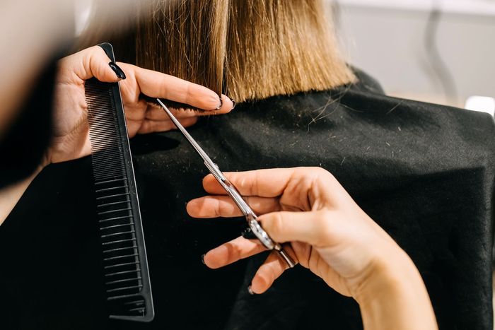 Coiffeuse coupant les cheveux blonds d'une cliente aux ciseaux et au peigne