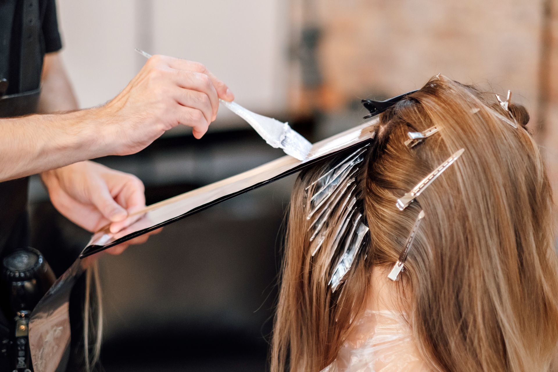 Coiffeuse appliquant une couleur au pinceau sur les mèches de cheveux d'une cliente