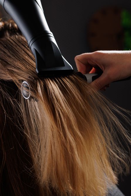 Main tenant un sèche-cheveux noir, soufflant une mèche de longs cheveux blonds dans un salon de coiffure