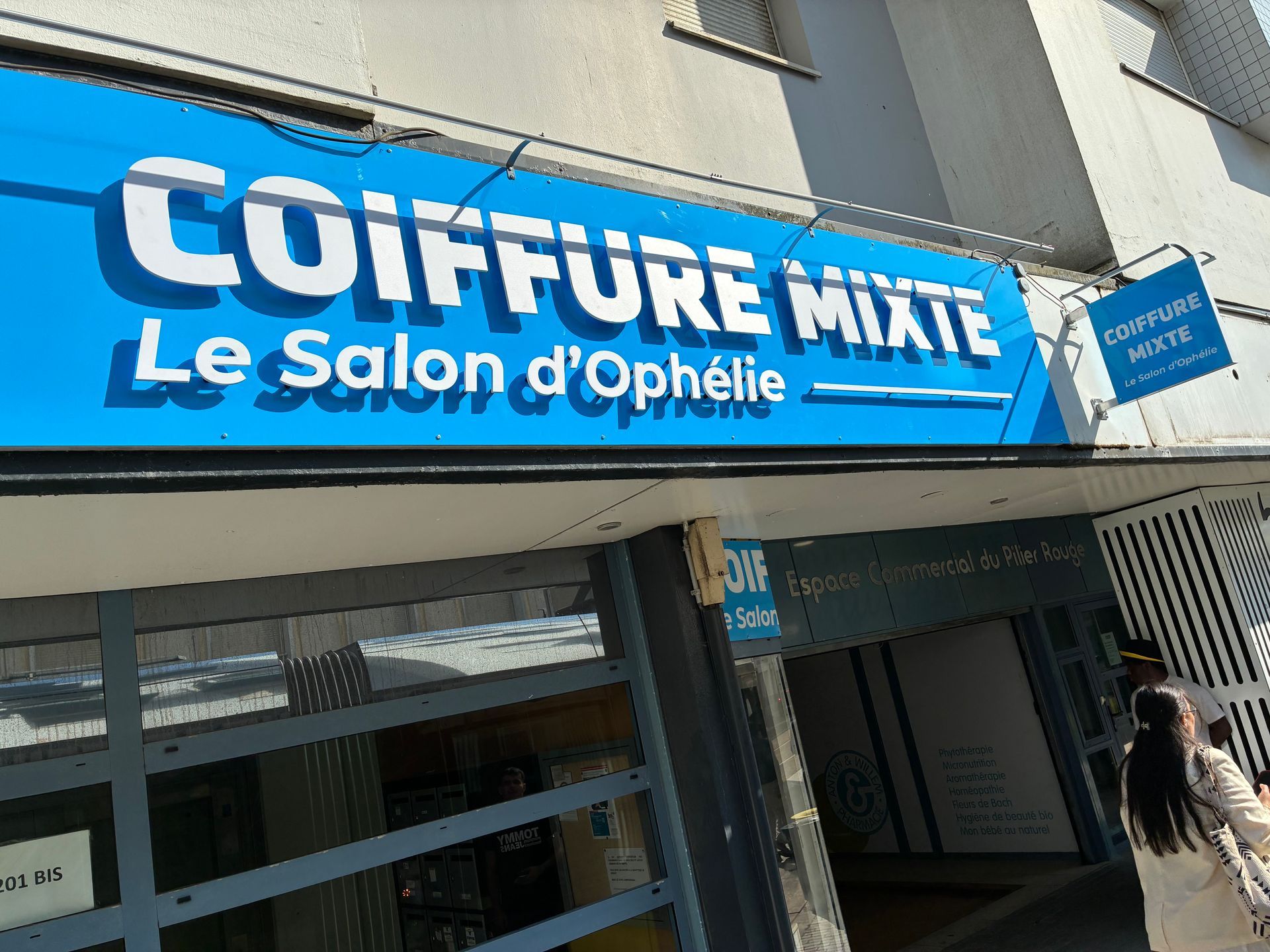 Enseigne bleue indiquant COIFFURE MIXTE – Le Salon d’Ophelie au-dessus de l’entrée d’un salon de coiffure