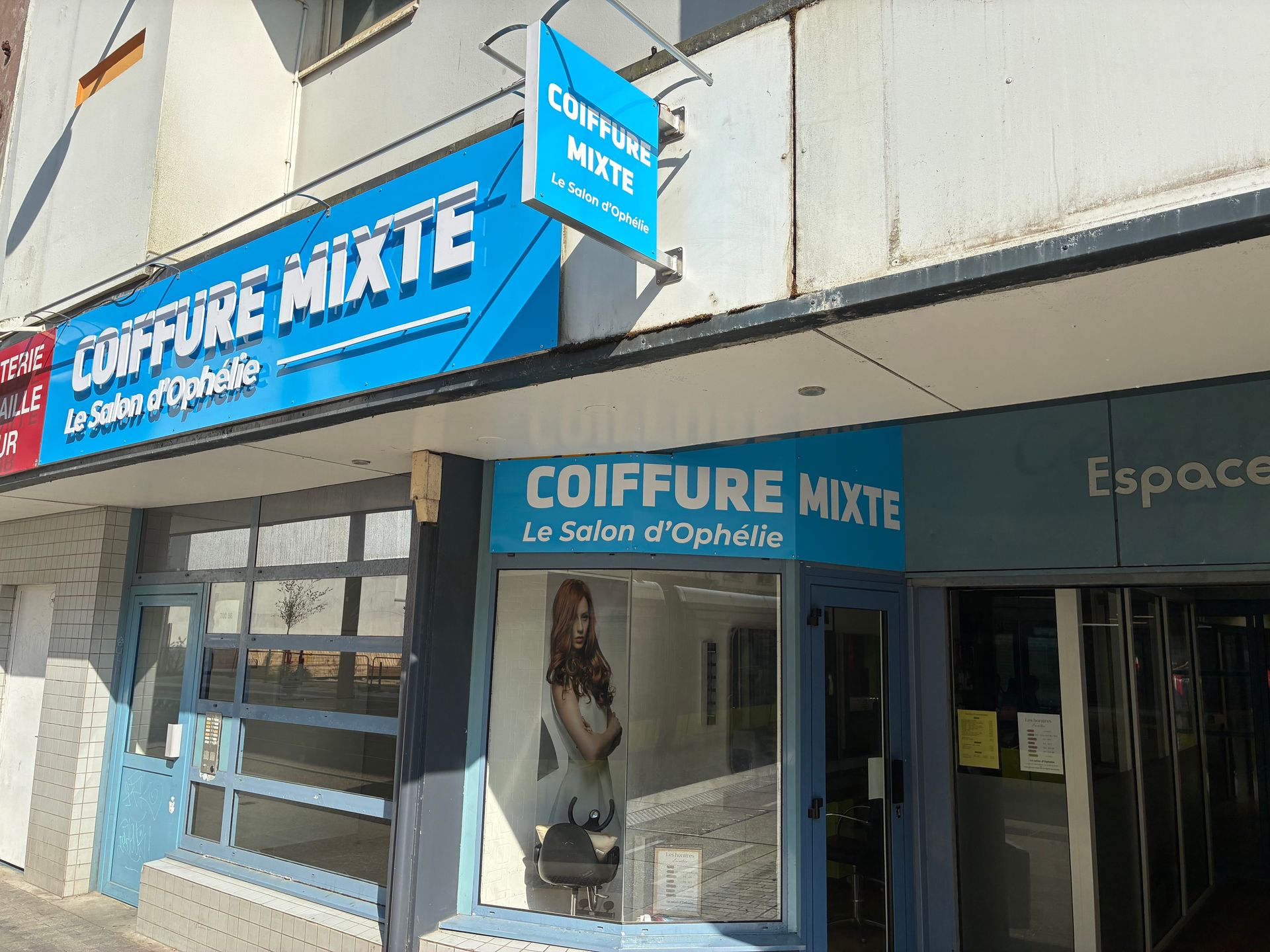 Enseigne bleue d’un salon de coiffure COIFFURE MIXTE à l’angle d’une rue