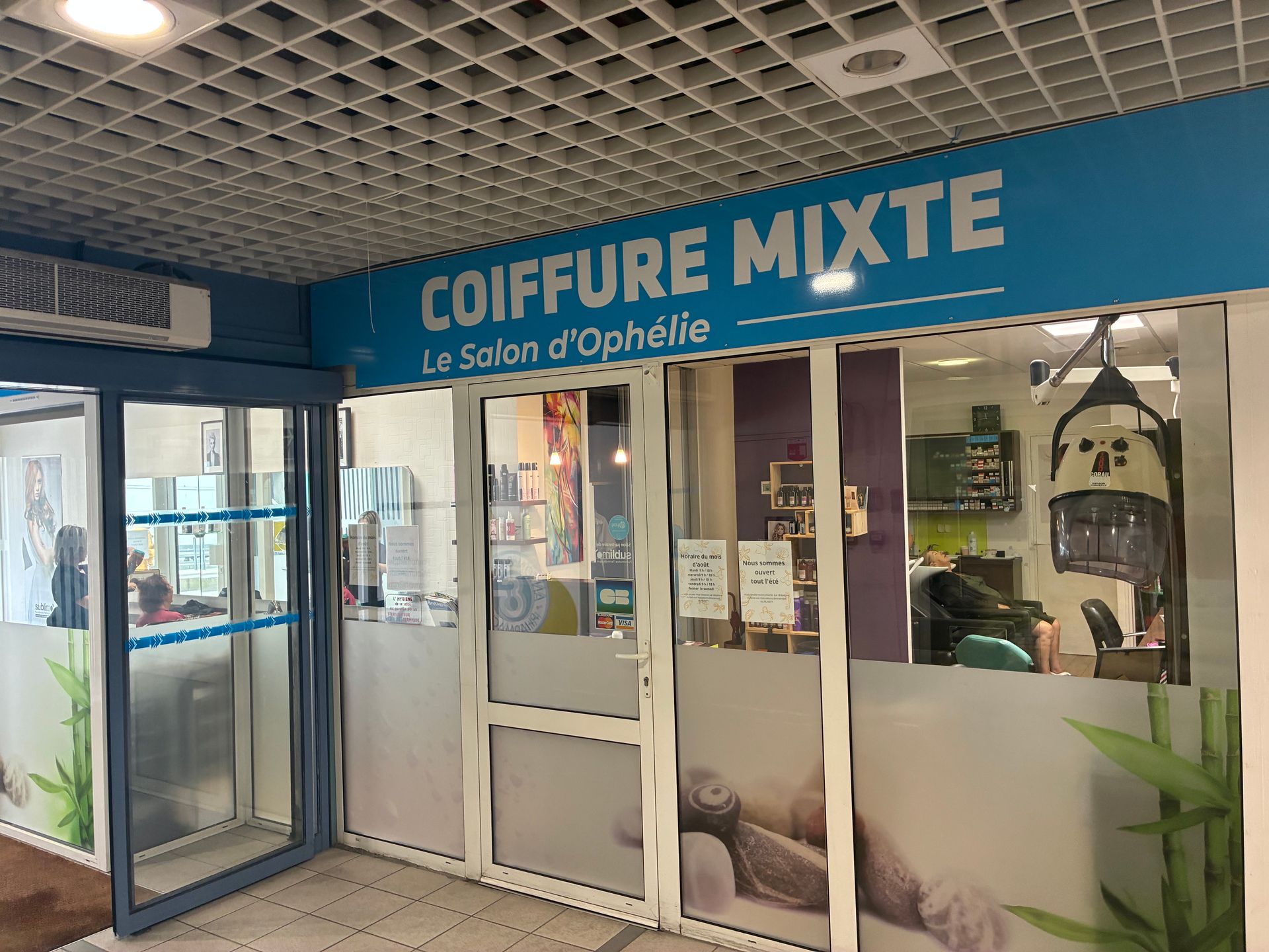 Devanture d’un salon de coiffure avec une enseigne bleue indiquant COIFFURE MIXTE et une entrée vitrée.