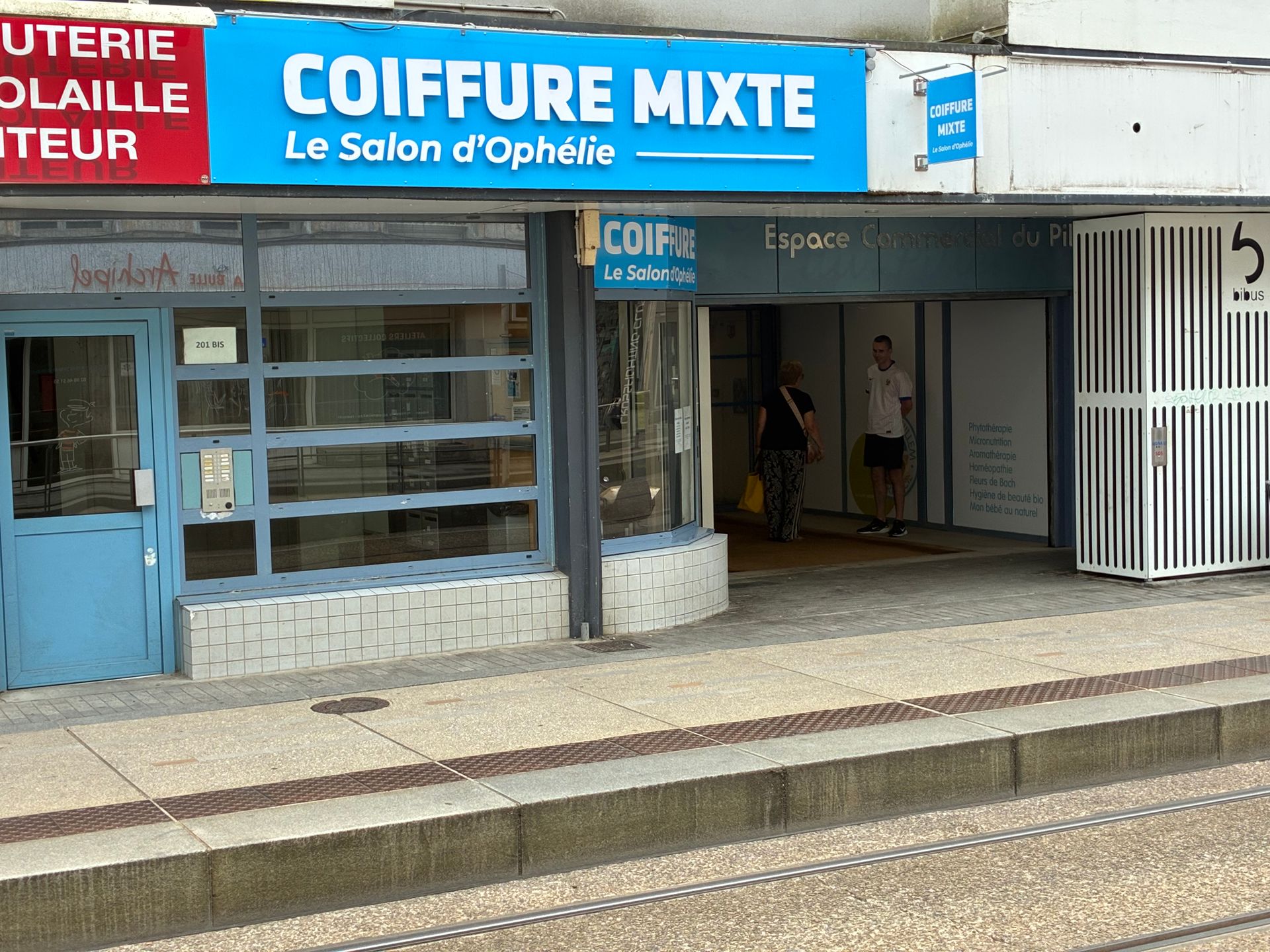 Devanture du salon de coiffure Coiffure Mixte, avec une enseigne bleue et des vitrines donnant sur le trottoir