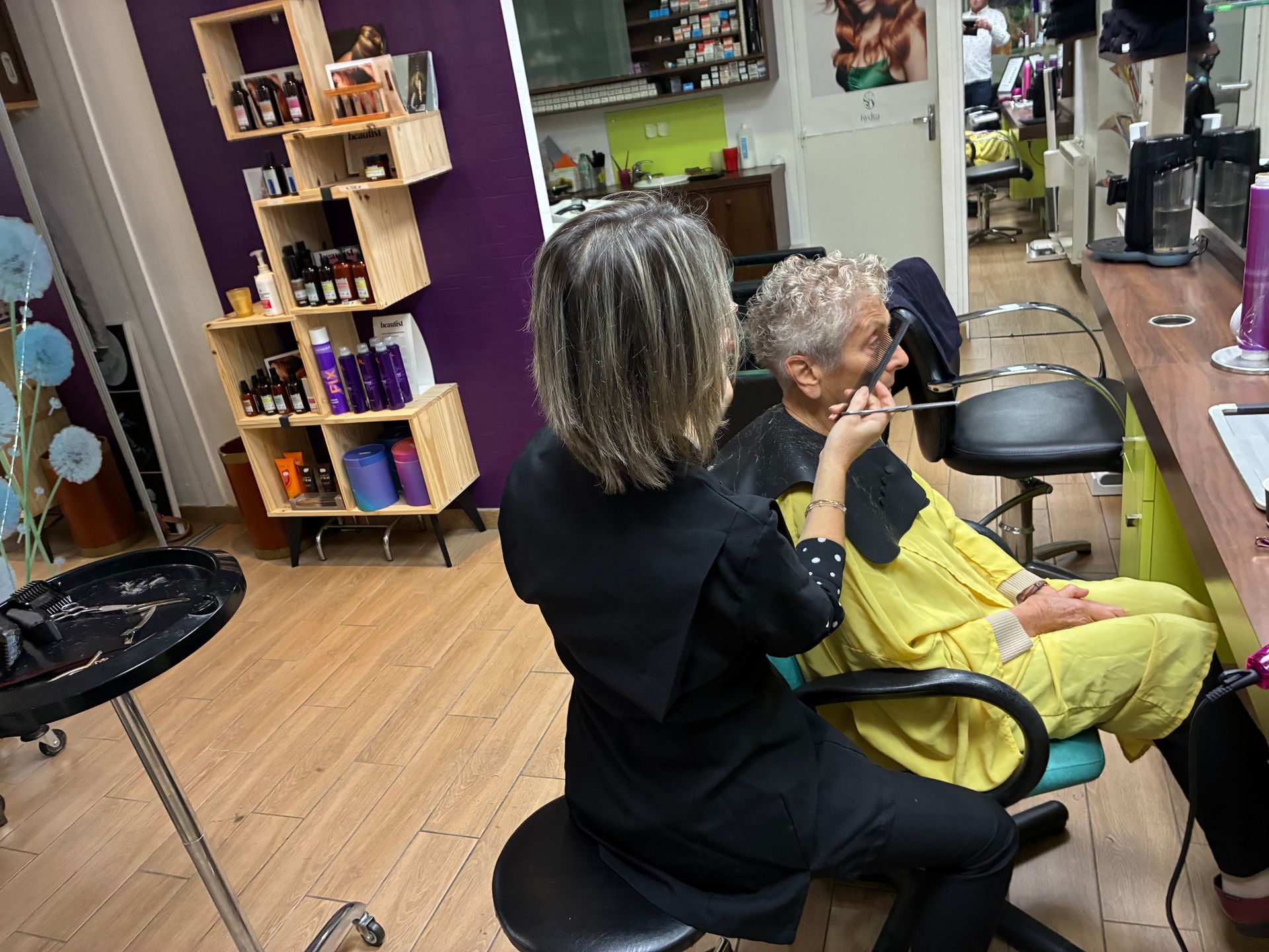 Scène dans un salon de coiffure : un coiffeur coupe les cheveux gris d’un client assis sur une chaise