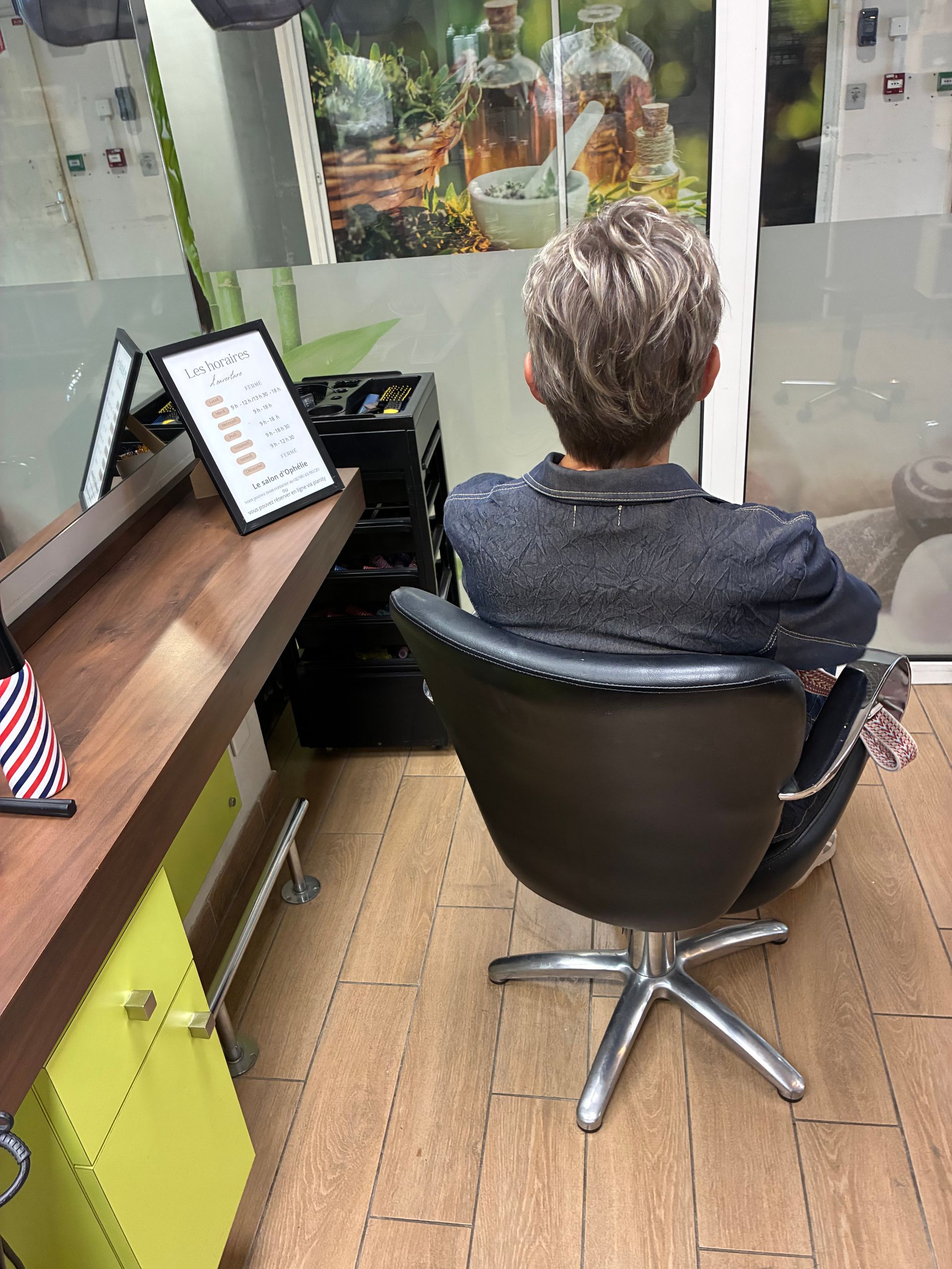 Personne assise sur une chaise de salon de manucure, face à une tablette, vue de dos.