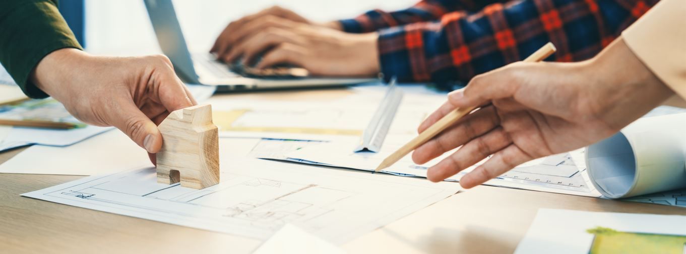 Personas colaborando en planos arquitectónicos con una casa modelo y una computadora portátil.