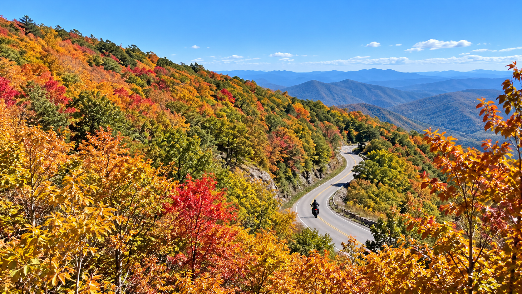 Winding mountain road through vibrant autumn foliage with a cyclist and blue ridges in the distance