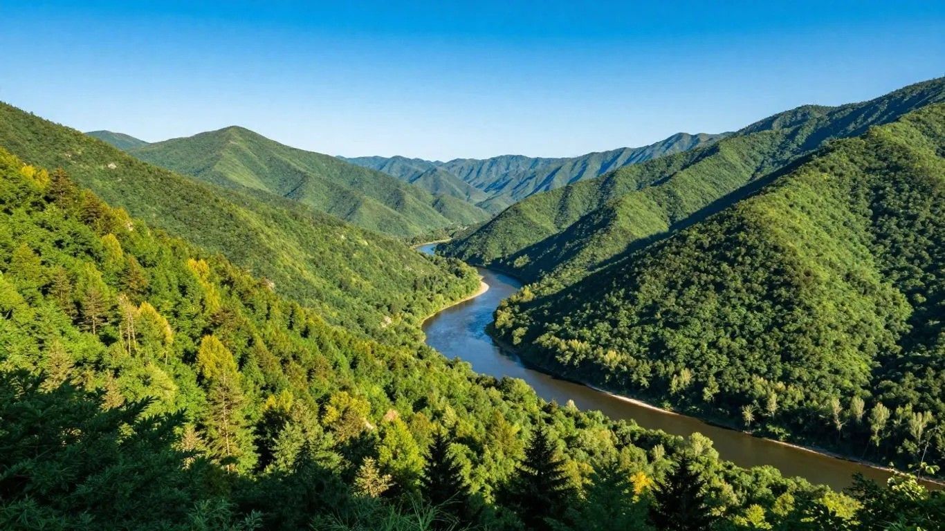 Green forested mountains surround a winding river under a bright blue sky.