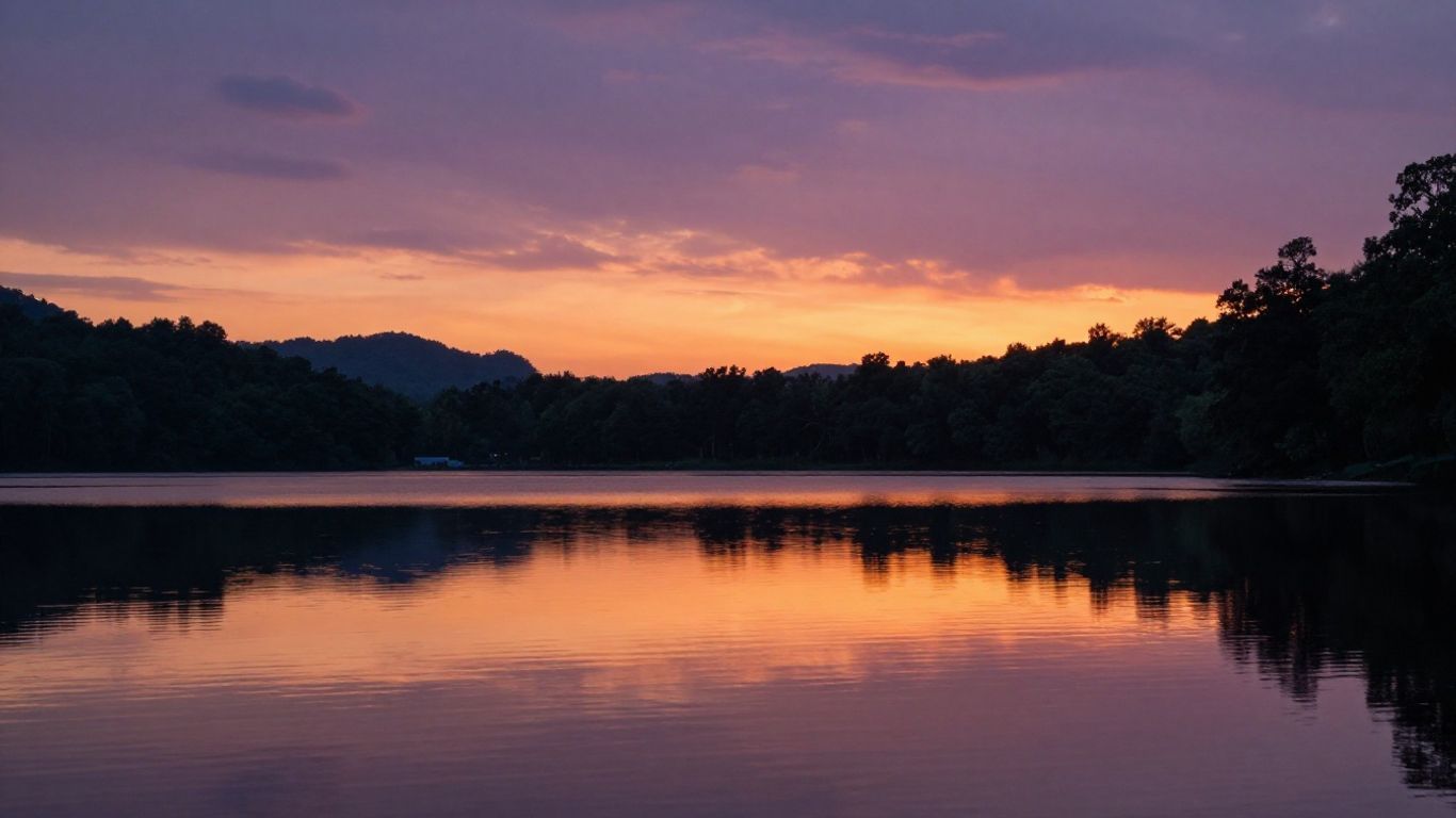 Sunset over a calm lake with silhouetted trees and mountains reflected in the water