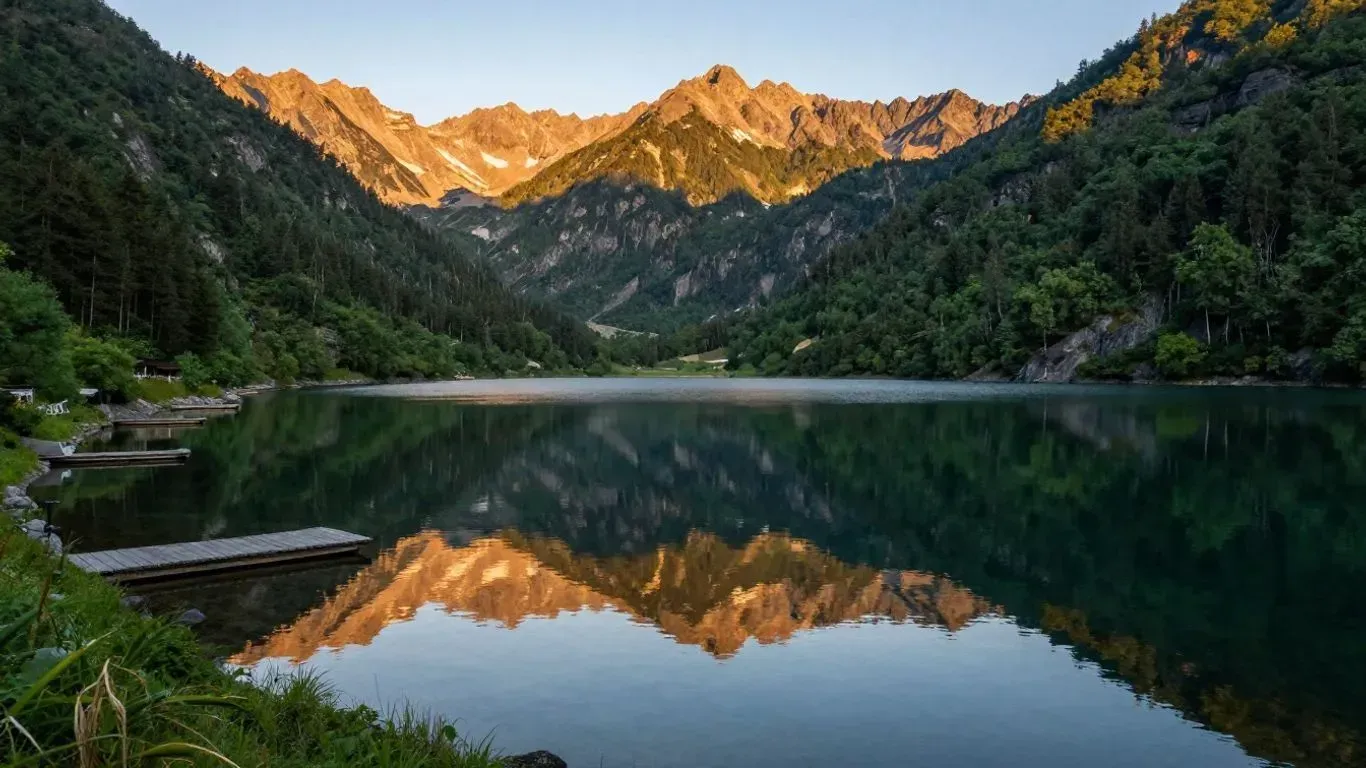 Mountain lake reflecting pine forest and sunlit peaks at sunset