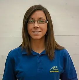 Une femme portant des lunettes et un polo bleu se tient devant un mur blanc.