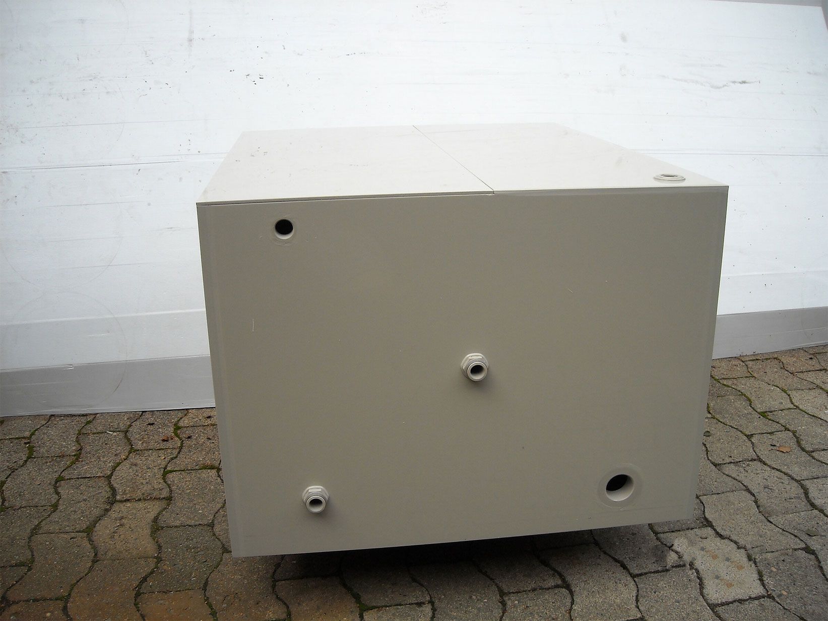 Eine weiße Kiste mit Löchern darin steht auf einem Ziegelboden