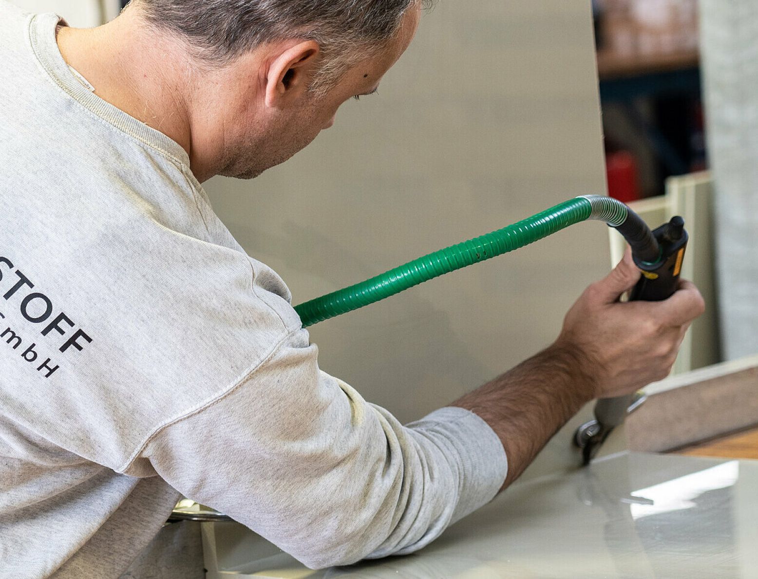 Ein Mann mit einem T-Shirt mit der Aufschrift „Stoff“ arbeitet an einem Stück Holz.