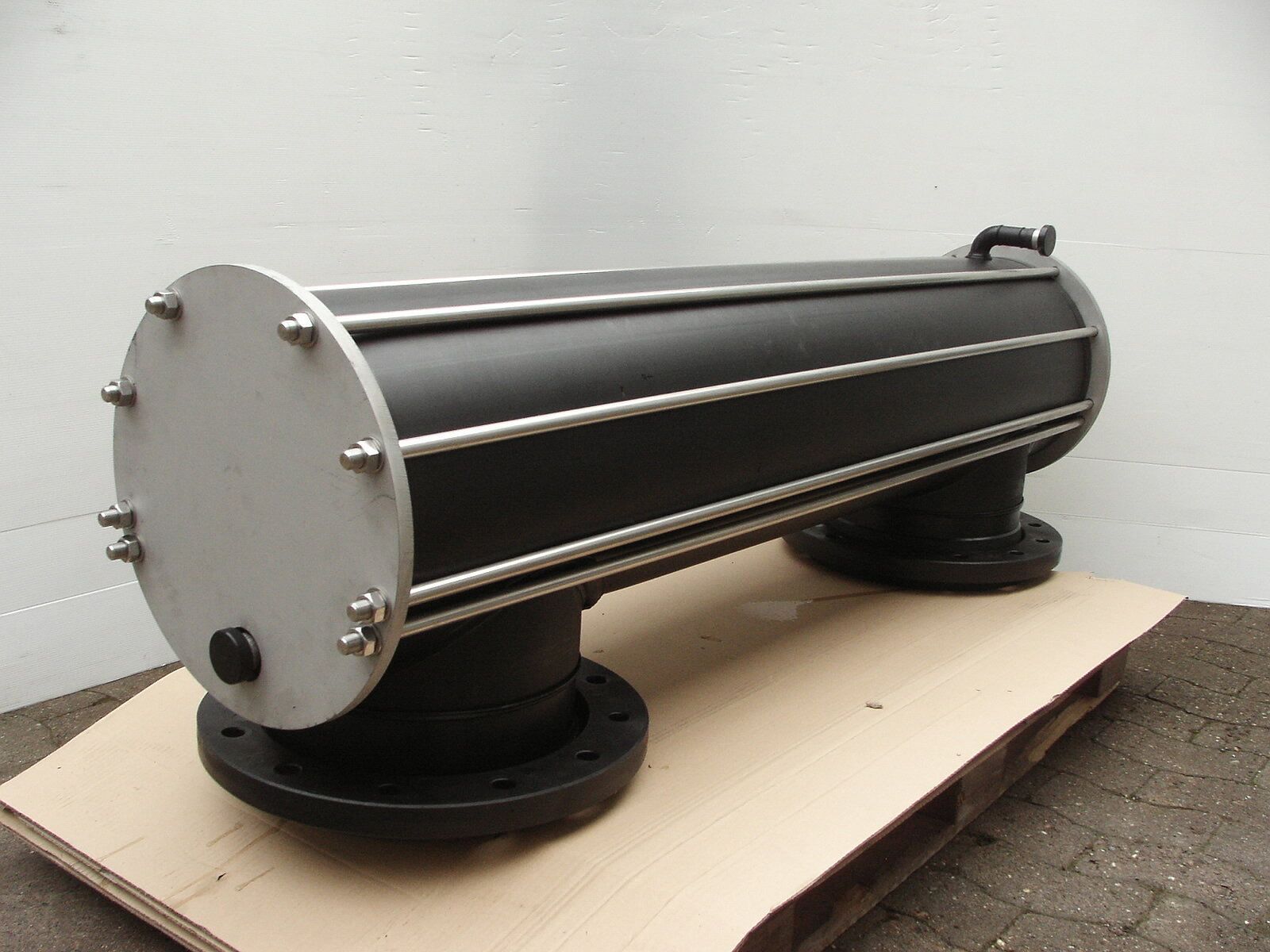 Auf einer Papppalette liegt ein großes schwarzes Rohr.