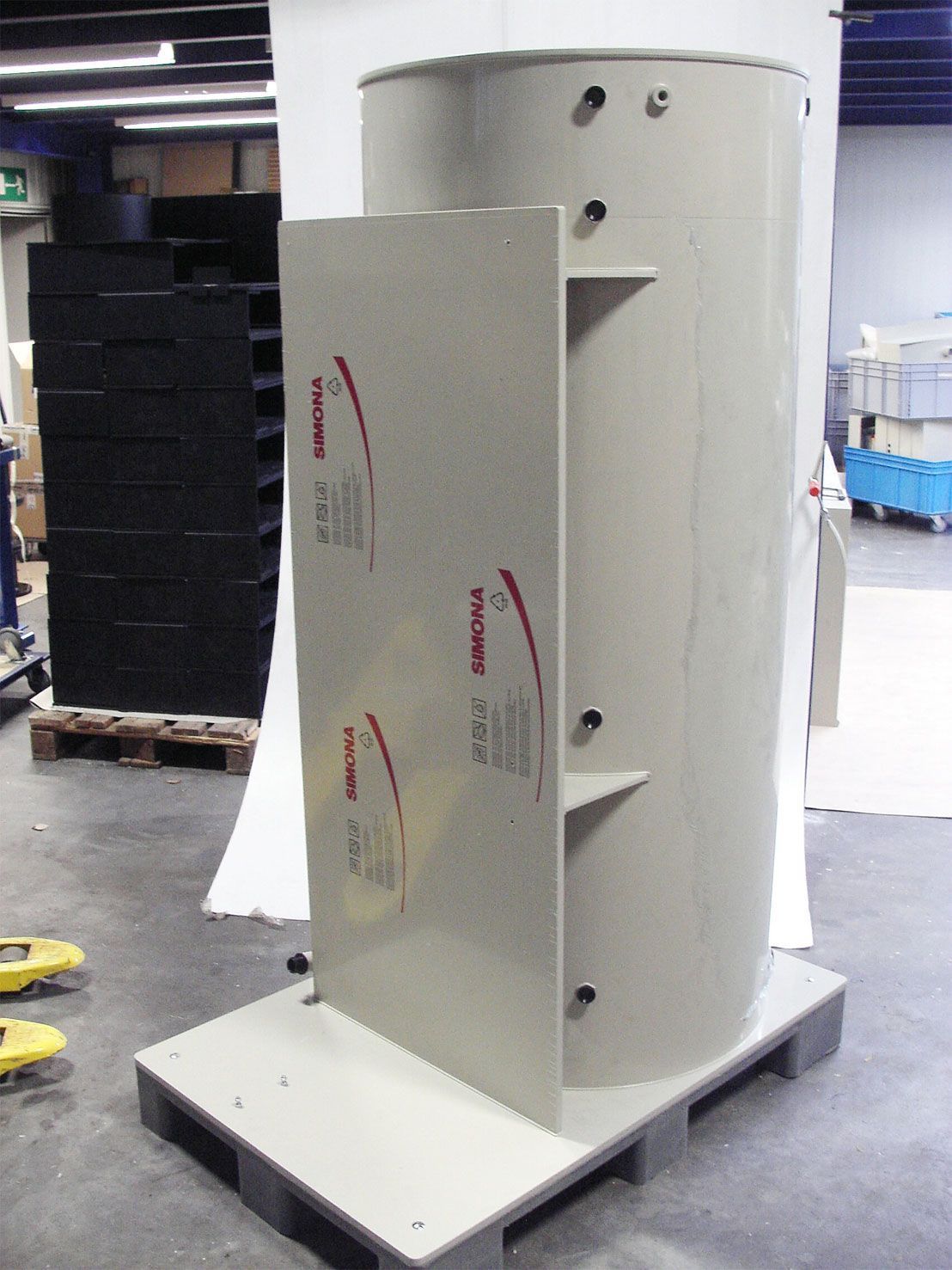 Ein großer weißer Zylinder mit einem roten Pfeil darauf steht auf einer Palette