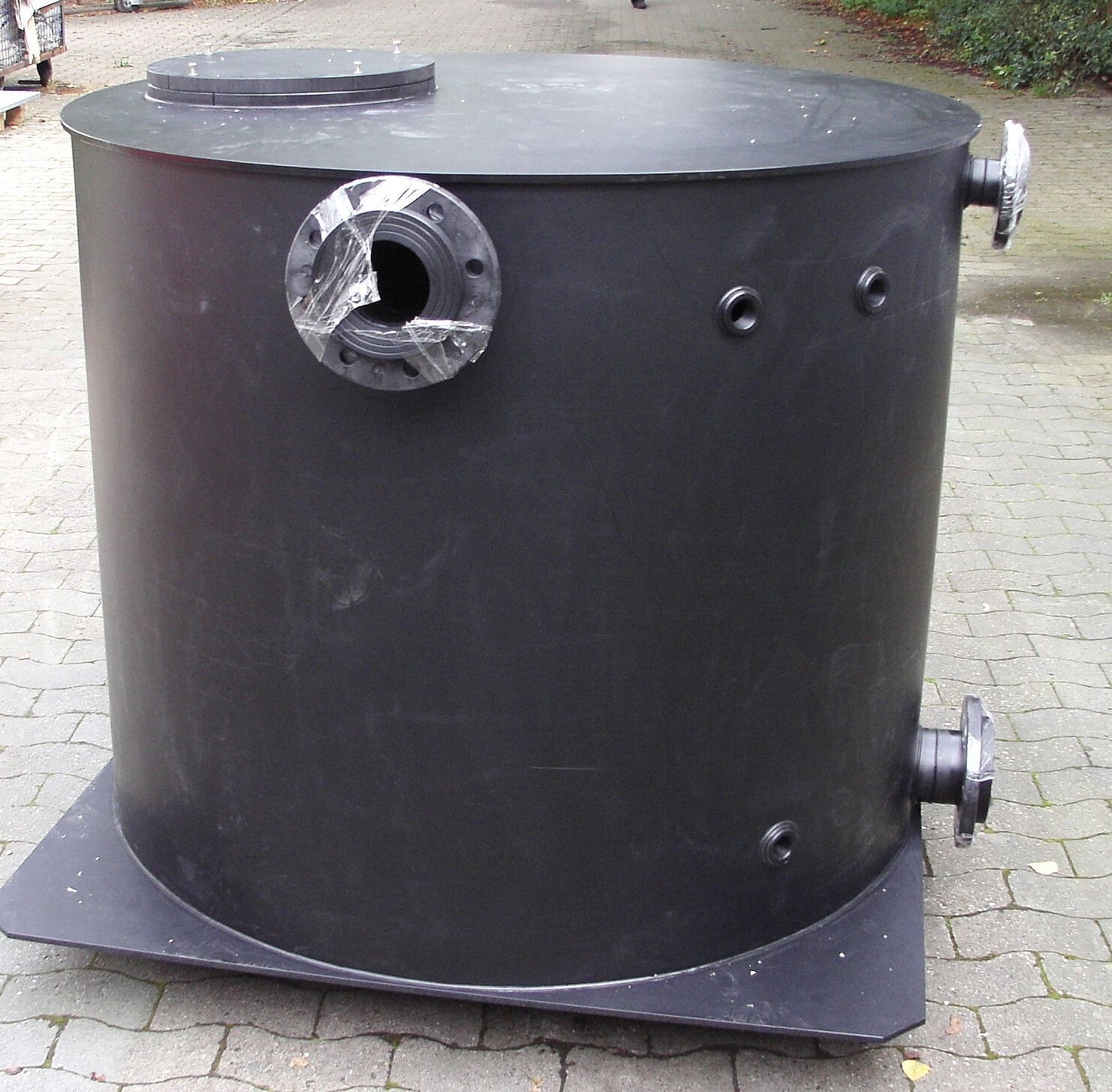 Ein großer schwarzer Zylinder steht auf einem gemauerten Gehweg