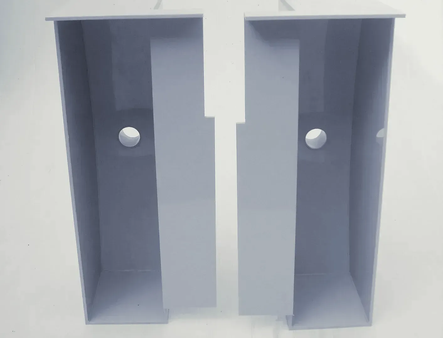 Zwei graue Kästen mit Löchern stehen nebeneinander auf einer weißen Fläche.