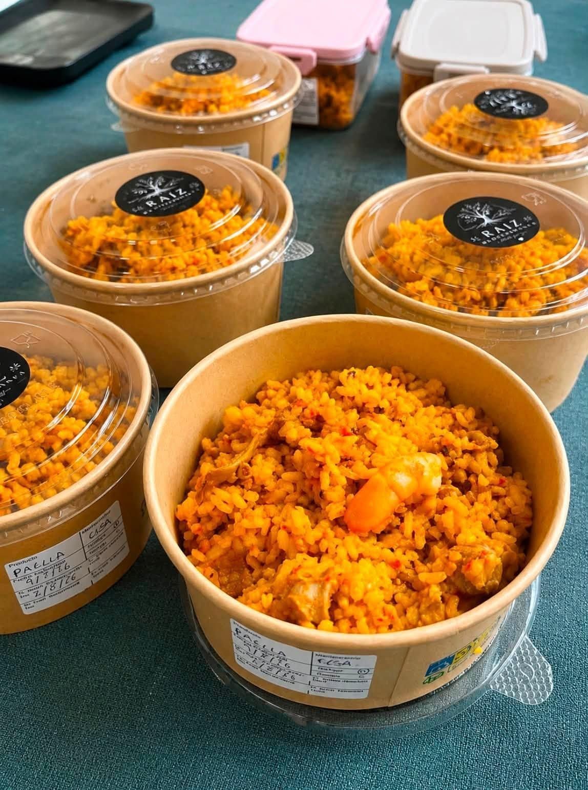 Varios cuencos de papel con comida naranja y desmenuzable, con tapas transparentes, sobre una mesa verde.