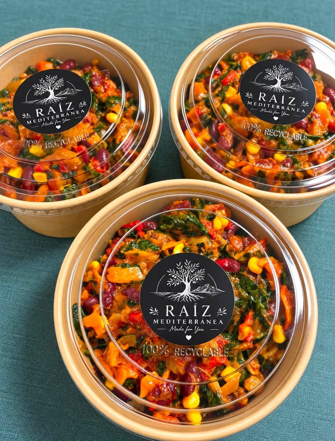 Tres recipientes transparentes de ensalada de frutas de colores, con etiquetas negras, sobre un fondo verde azulado