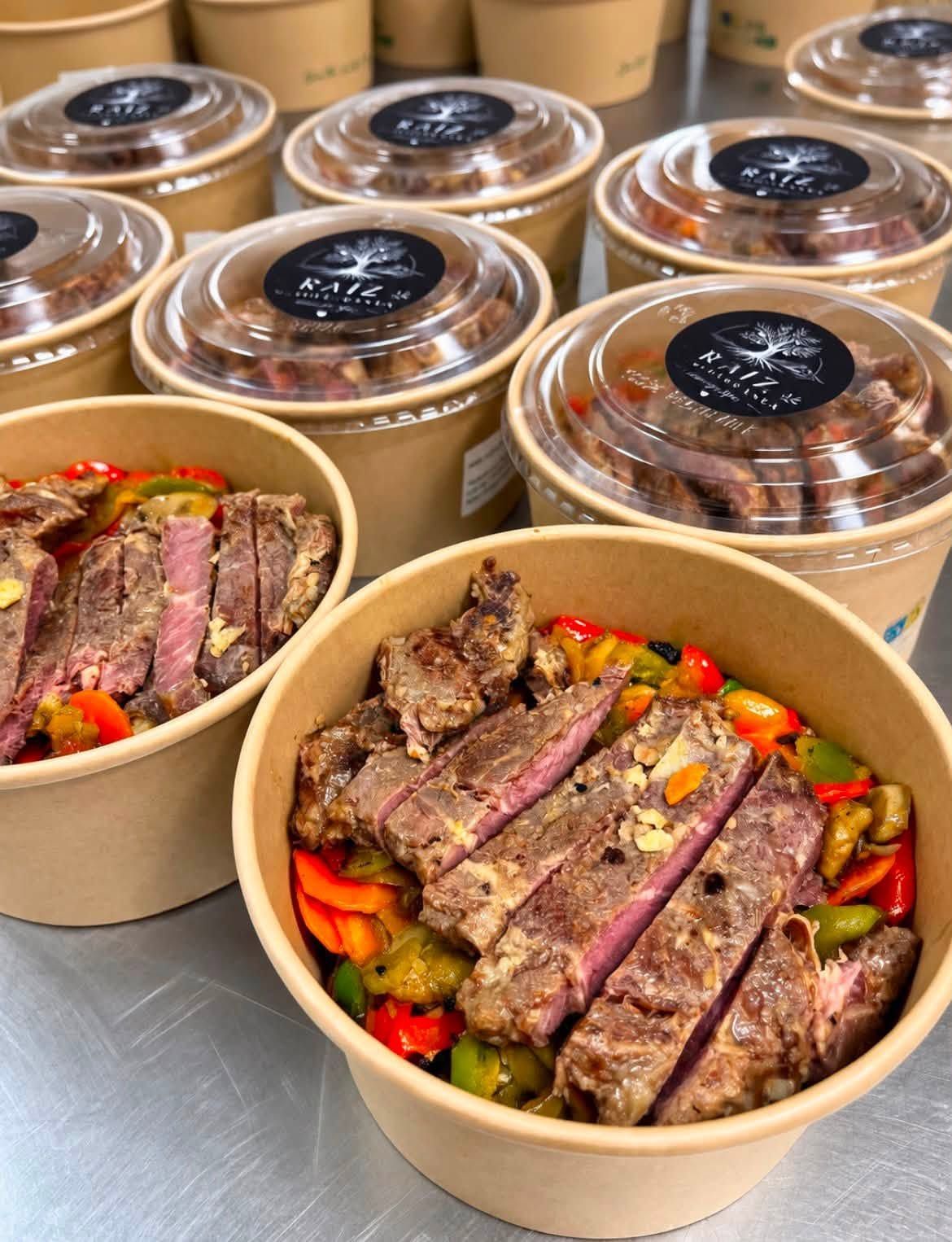 Cuencos para llevar con filete en tiras y verduras de colores, apilados al fondo