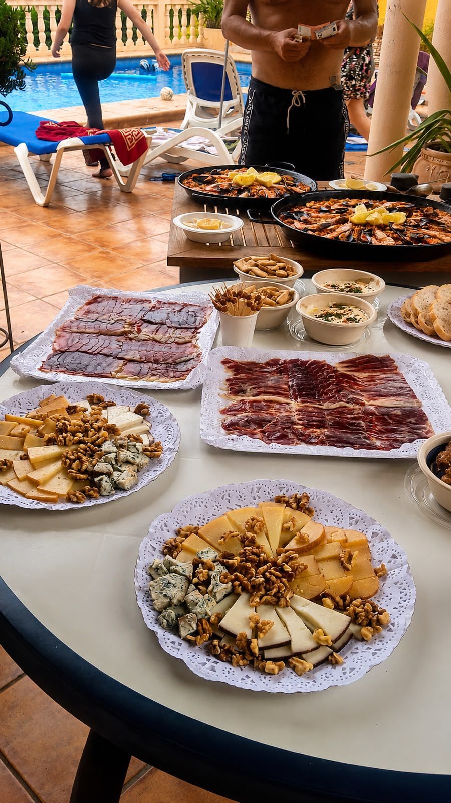 Mesa de bufé con una variedad de pasteles y aperitivos en bandejas blancas junto a una terraza con piscina