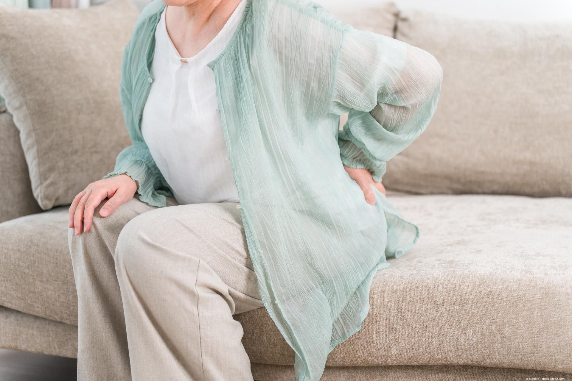 Eine ältere Frau hält sich im Sitzen ihren unteren Rücken