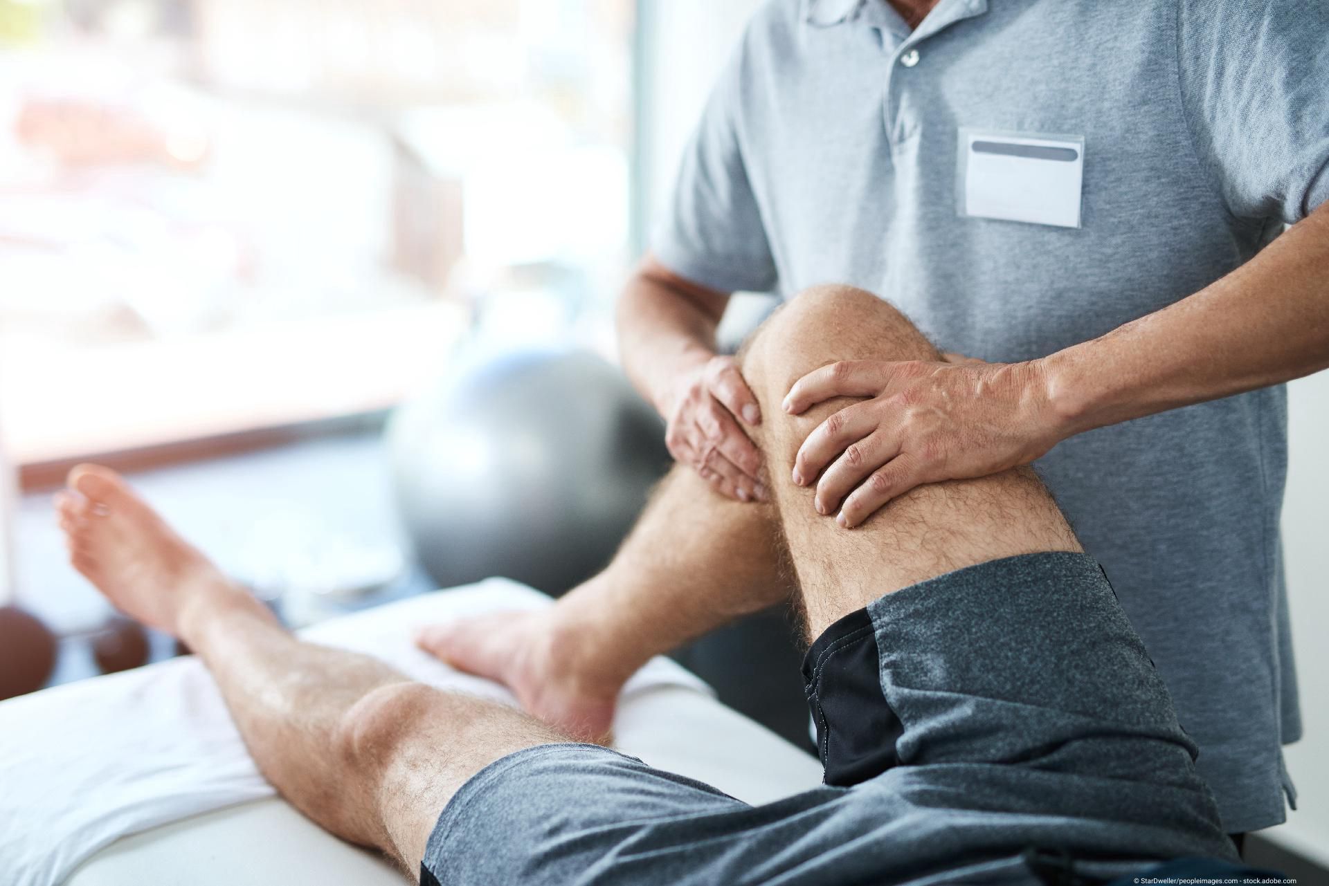 Therapeut/Arzt greift das Knie eines Patienten