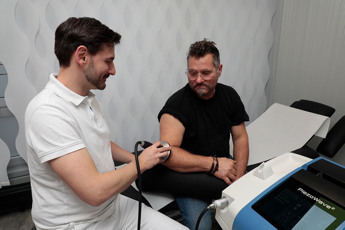 Dr. von Hoegen wendet ein Gerät zur Therapie am Ellenbogen eines Patienten an