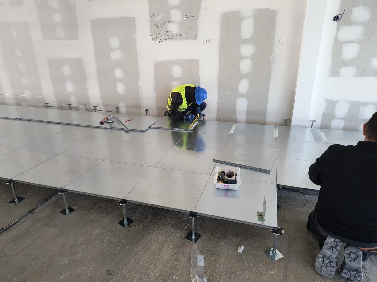 Un gran vestíbulo bañado por el sol con grandes ventanales, suelos de mármol, plantas en macetas y una mesa central que se refleja en el suelo brillante.
