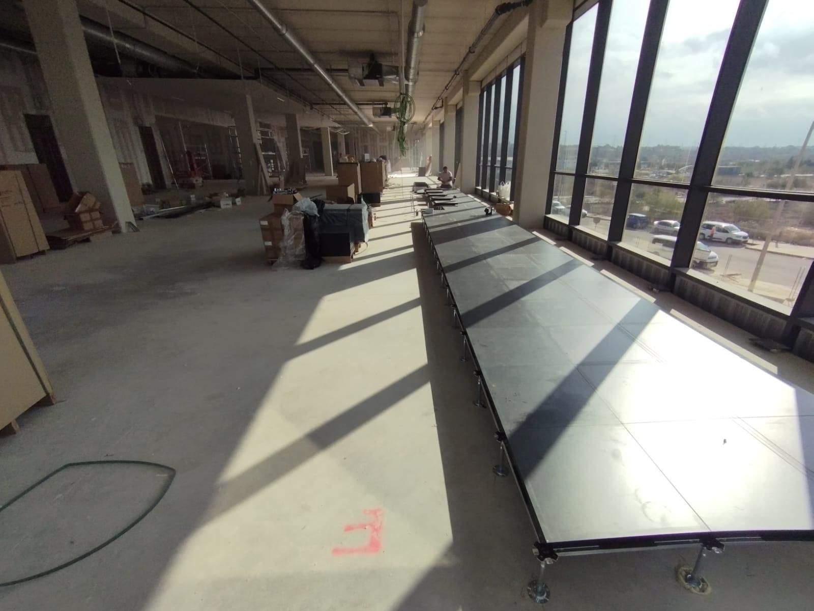 Un gran vestíbulo bañado por el sol con grandes ventanales, suelos de mármol, plantas en macetas y una mesa central que se refleja en el suelo brillante.