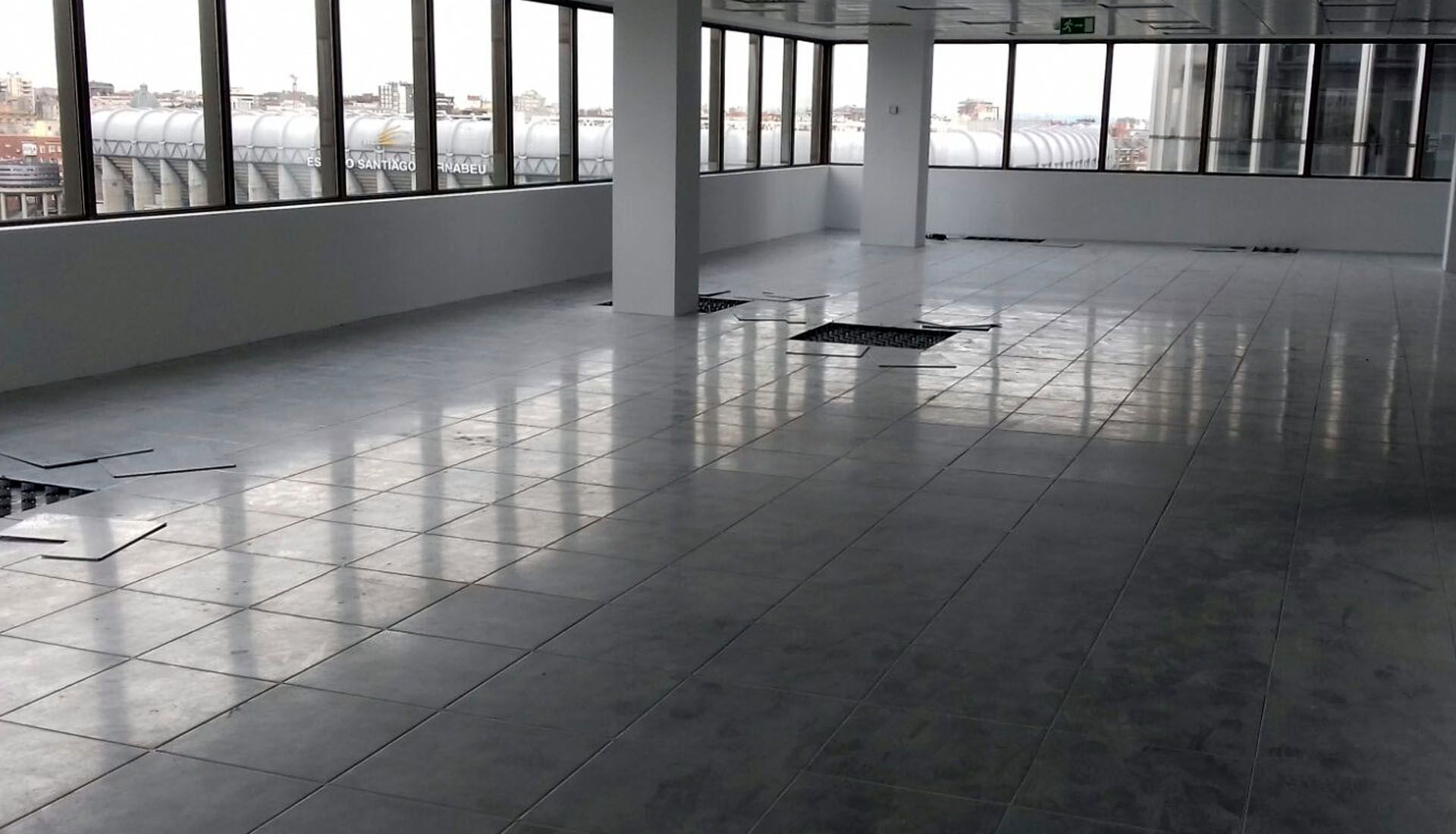 Habitación vacía con azulejos, grandes ventanales y una columna blanca que refleja la luz en el suelo.