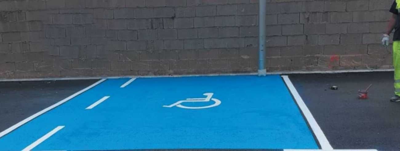 Un hombre está pintando un espacio de estacionamiento para discapacitados en un estacionamiento.