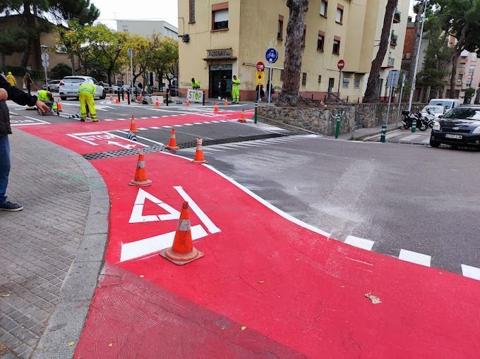 Un hombre está parado en una acera al lado de una carretera roja.