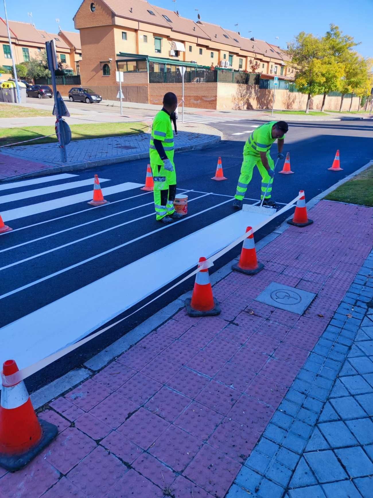 Dos hombres están pintando un paso de peatones al costado de la carretera.