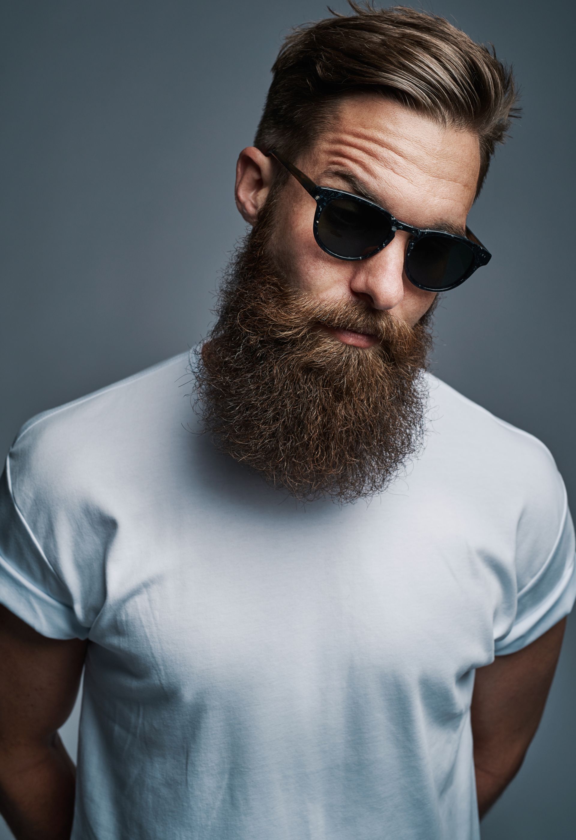 Homme barbu portant des lunettes de soleil et un tee-shirt blanc sur fond gris