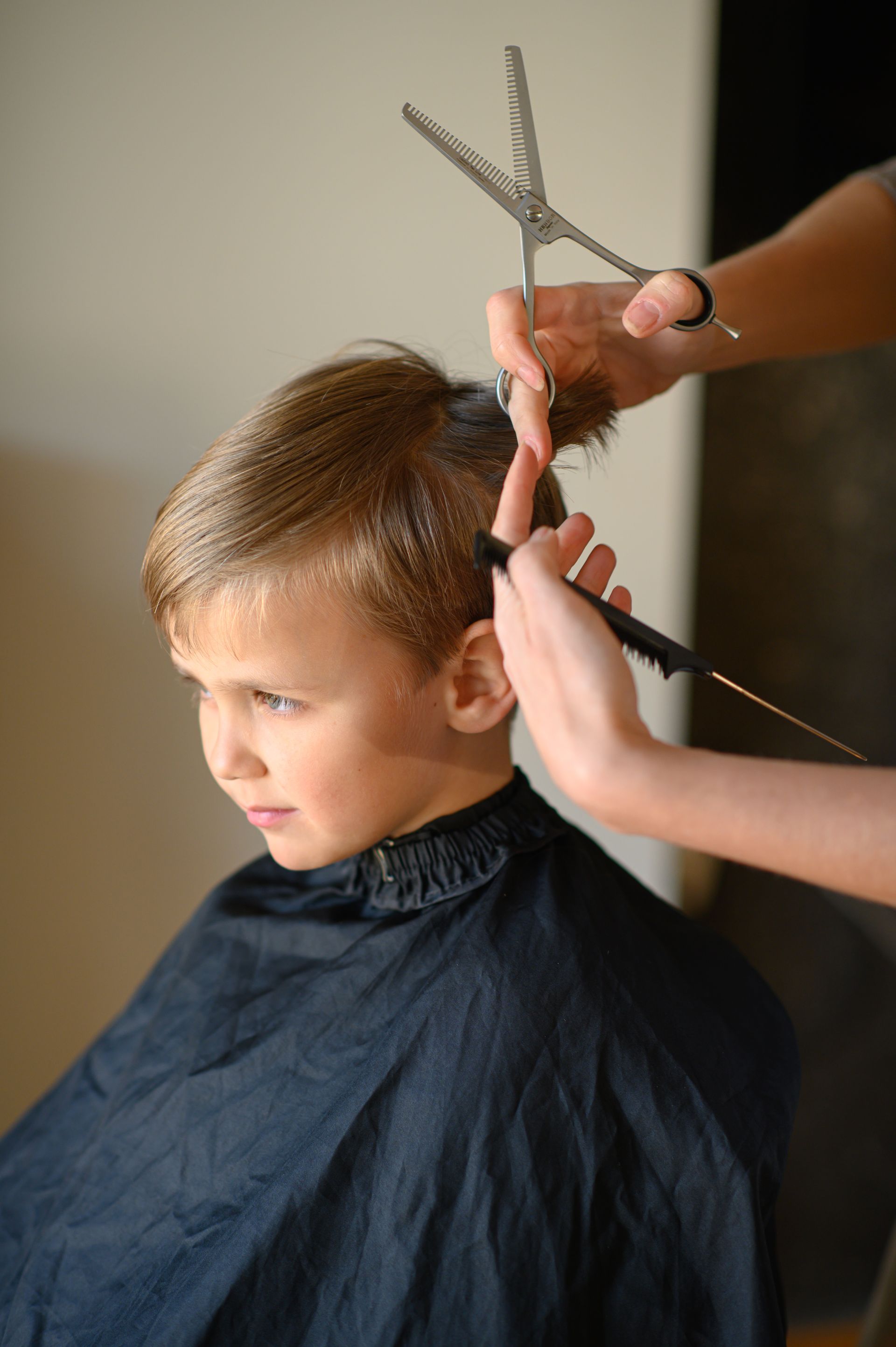 Un enfant se fait couper les cheveux par un coiffeur qui utilise des ciseaux et un peigne.