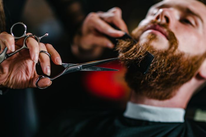 Gros plan d'un coiffeur taillant la barbe d'un homme barbu avec des ciseaux dans un salon de coiffure
