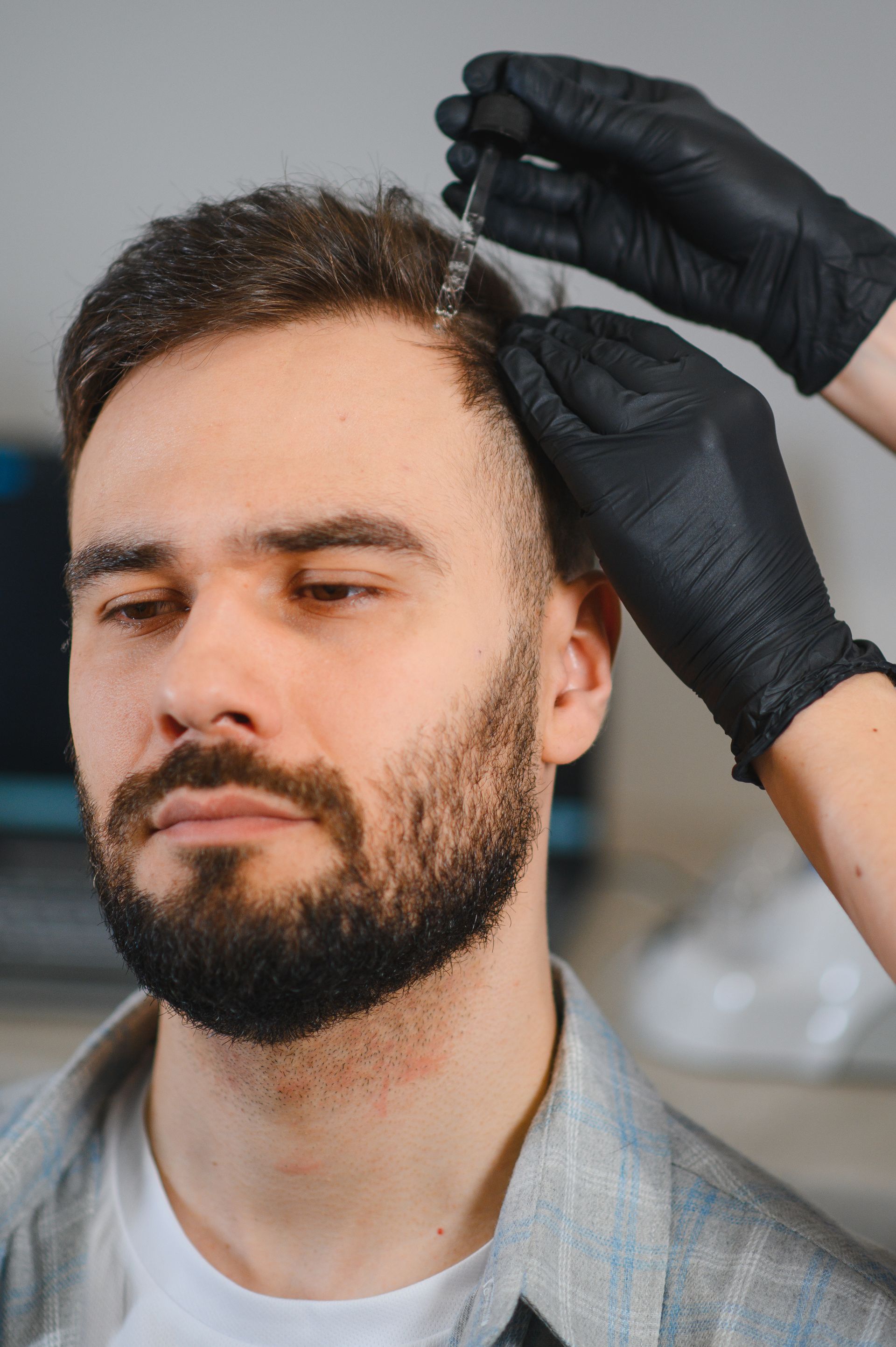 Des mains gantées appliquent un soin capillaire à un homme aux cheveux châtain.