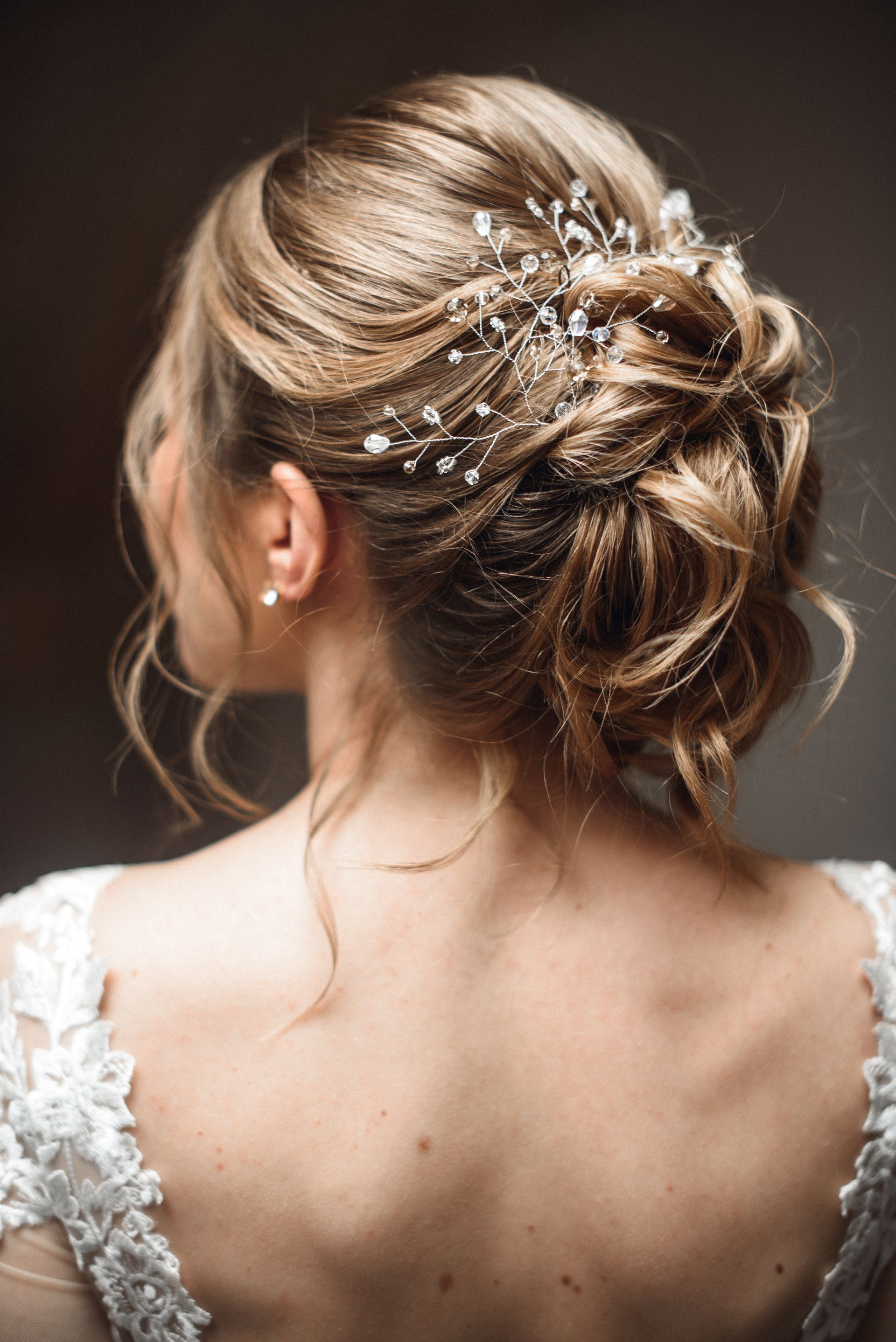 Coiffure d'un chignon avec des boucles blondes orné d'épingles à cheveux en perles, vue de dos.