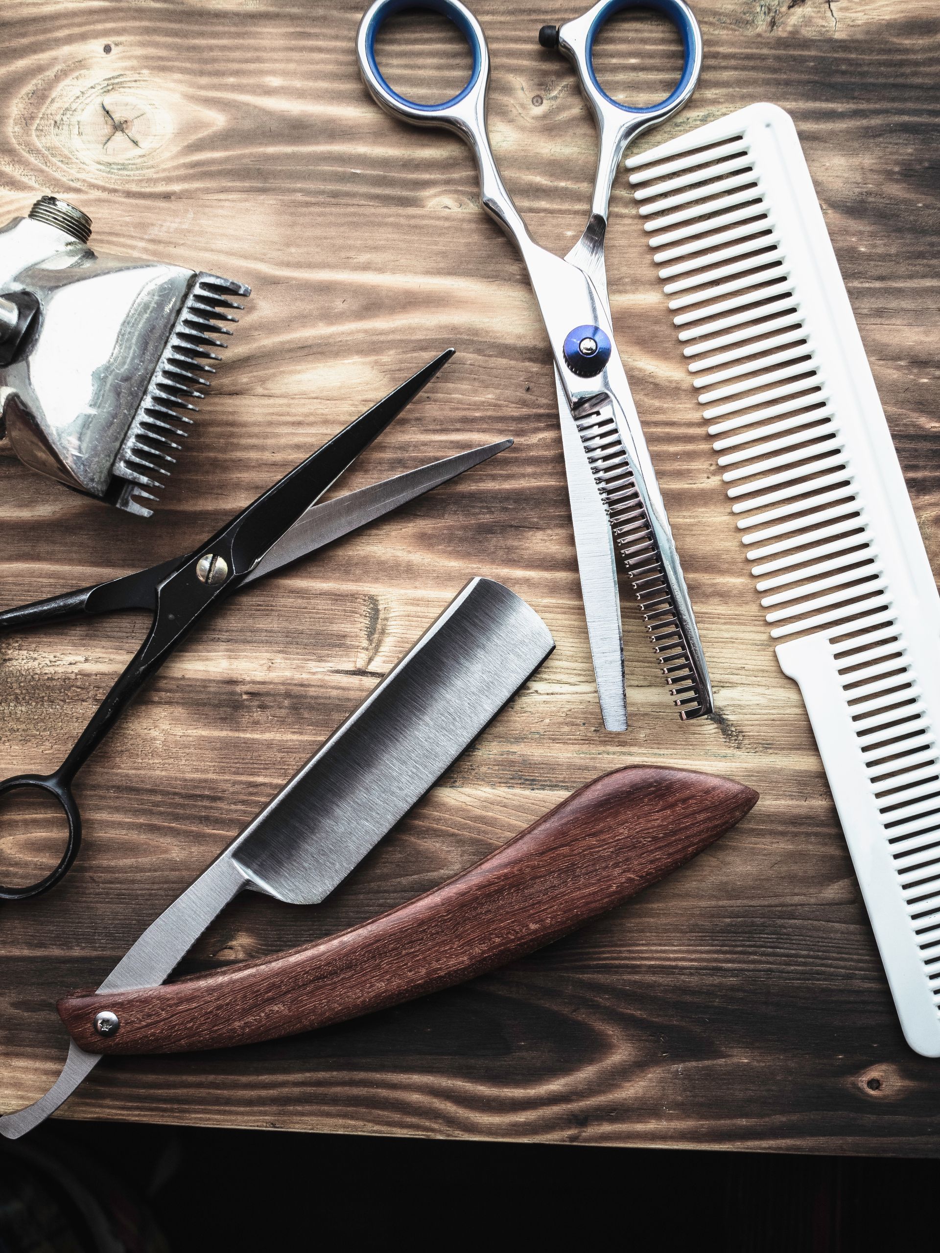 Outils de coiffure sur une table en bois : ciseaux, peigne, rasoir et brosse.