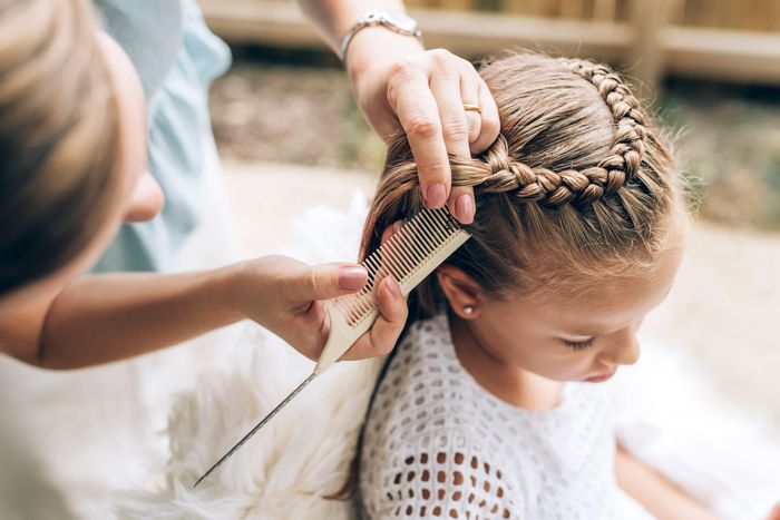 Dans un salon lumineux, une coiffeuse tresse les cheveux d'un enfant à l'aide d'un peigne.