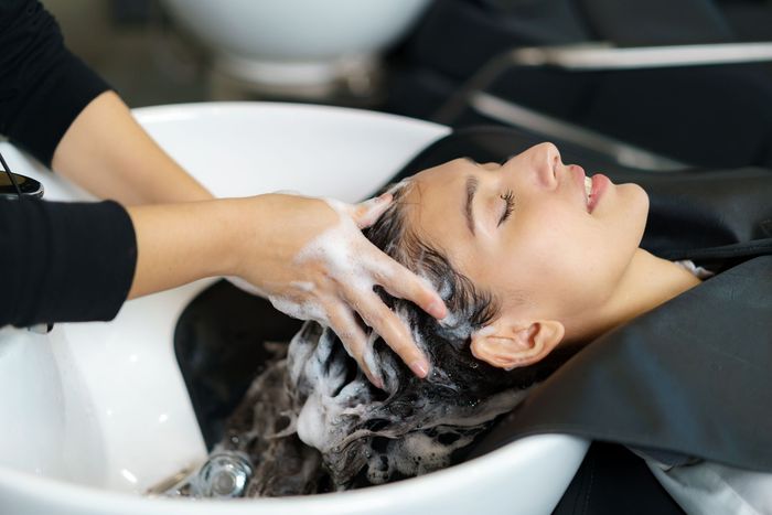 Lavage de cheveux au lavabo d'un salon de coiffure, les mains massent le shampoing sur les cheveux d'une cliente allongée.