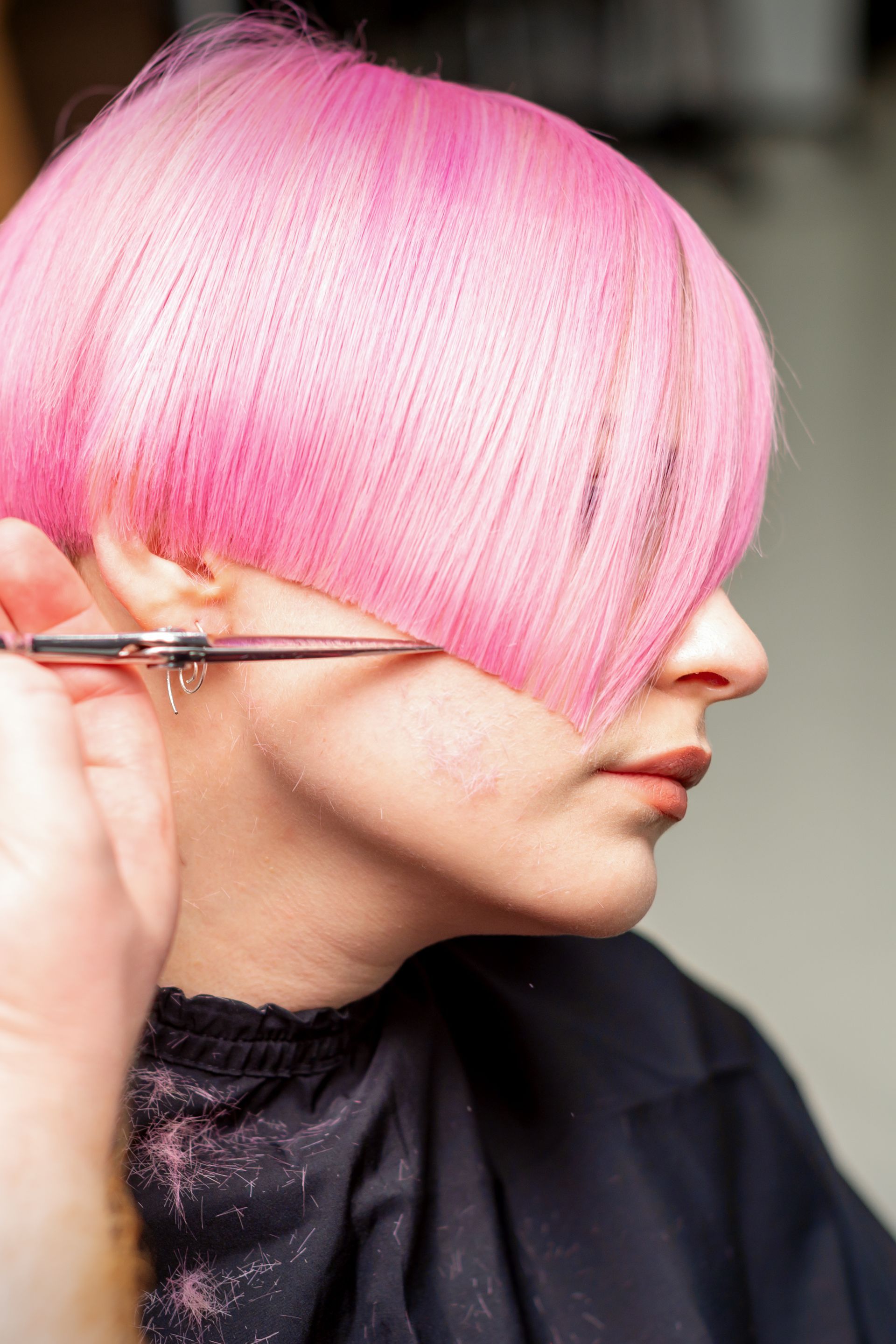Gros plan sur le profil d'une personne aux cheveux coupés au carré rose vif, taillés aux ciseaux.