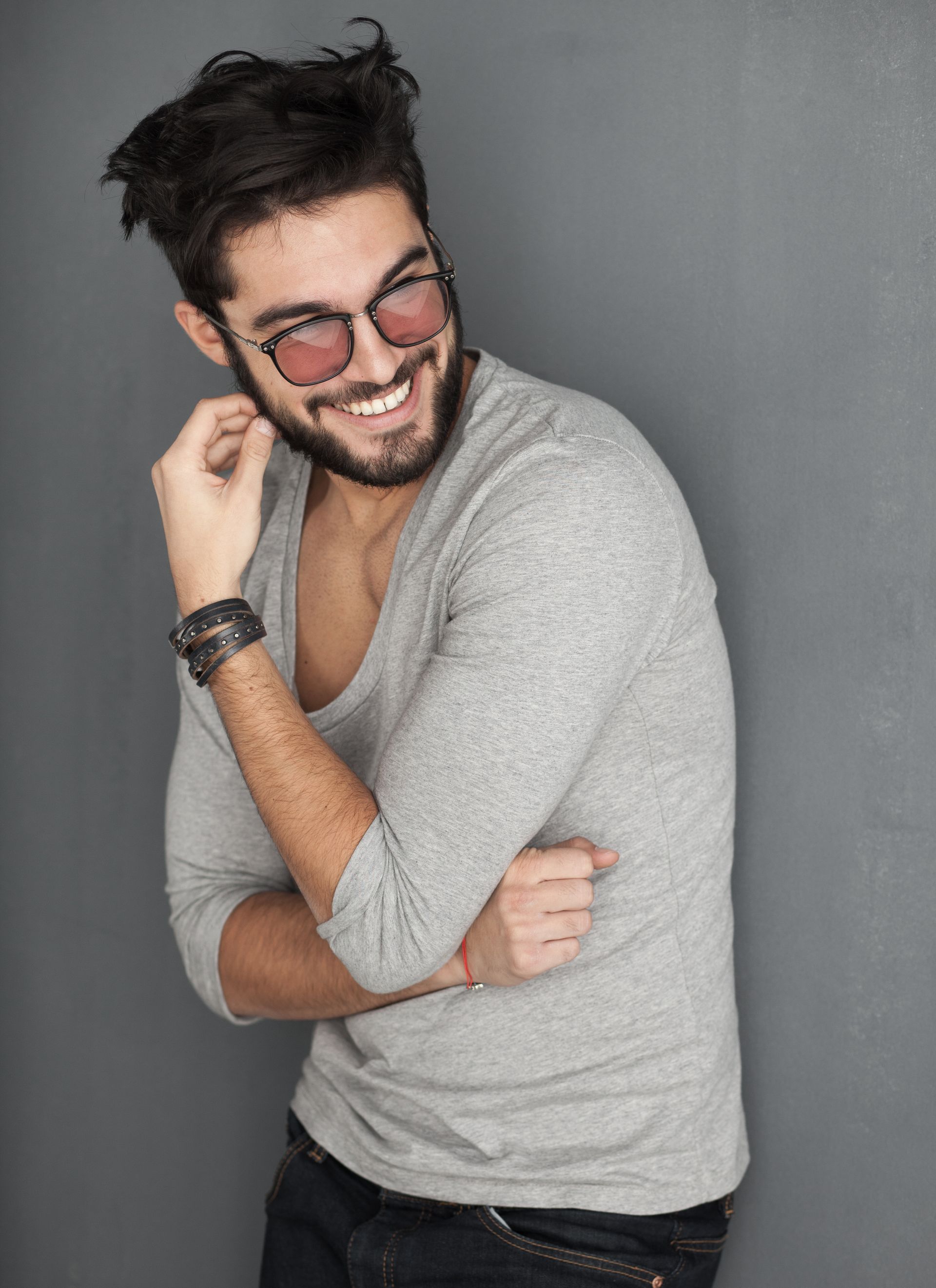 Homme souriant portant des lunettes et un pull gris, posant sur fond gris
