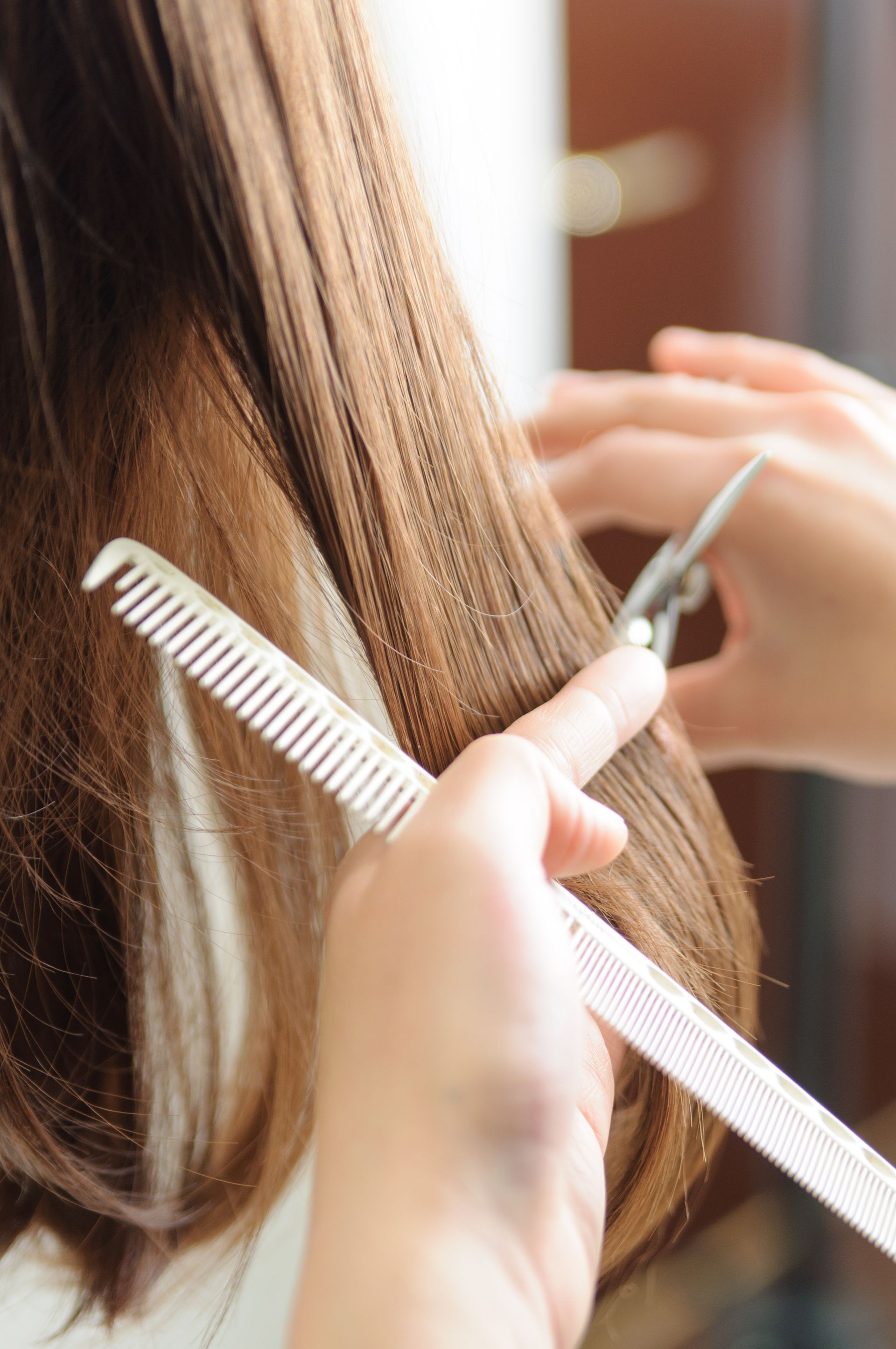 Gros plan sur des mains peignant de longs cheveux châtains tout en les coupant aux ciseaux