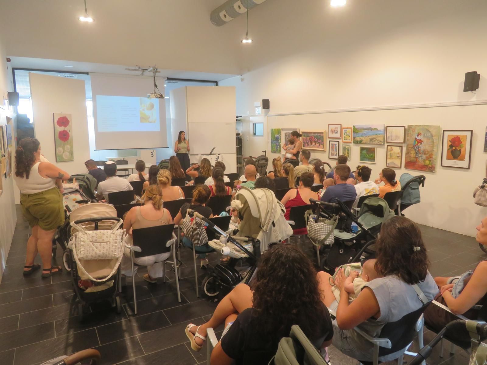 Público sentado en una sala de exposiciones viendo una presentación en una pantalla proyectada.