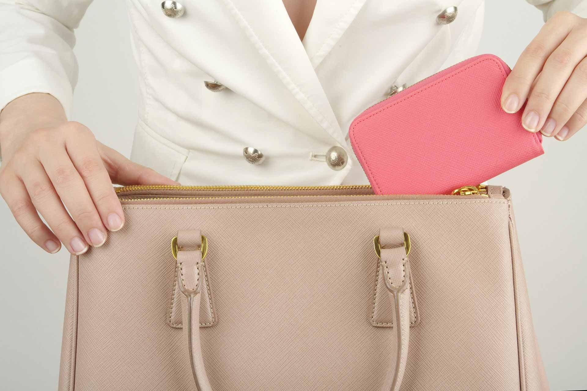 Una mujer está metiendo una billetera rosa en su bolso.